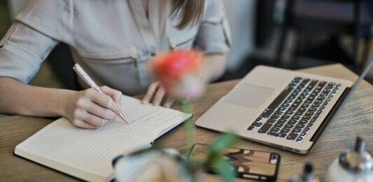 person writing on a notebook beside macbook