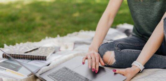 anonymous lady using laptop for studies in sunny park