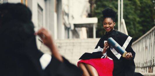 woman wearing black graduation coat sits on stairs